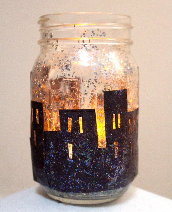 Make this magnificent DIY snowy skyline winter lantern - don't you love how the light shines though the windows on this recycled mason jar craft?