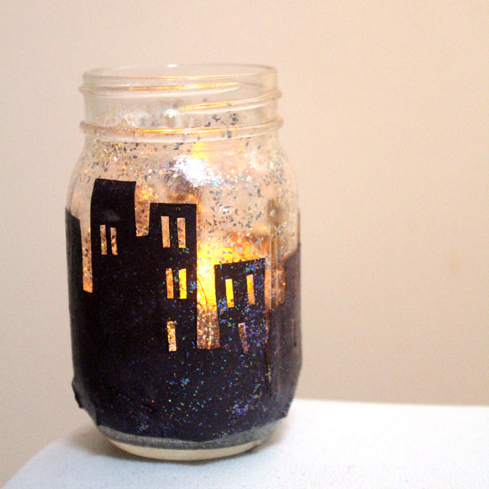 Make this magnificent DIY snowy skyline winter lantern - don't you love how the light shines though the windows on this recycled mason jar craft?