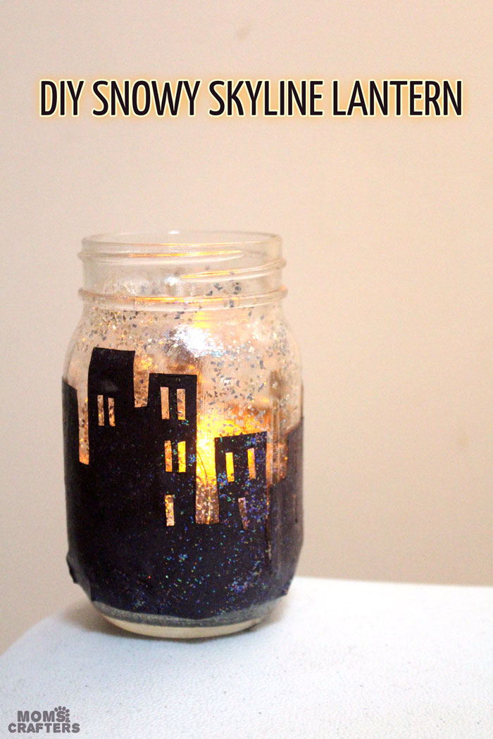 Make this magnificent DIY snowy skyline winter lantern - don't you love how the light shines though the windows on this recycled mason jar craft?