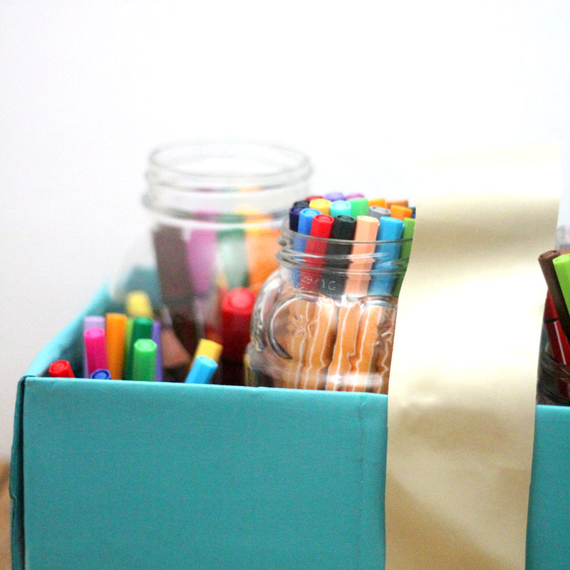 Make a super easy upcycled DIY marker storage caddy to transport the entire family's art supplies from the closet to the table in a usable bin! The jars can be removed individually to easily set up and clean up a family art station with coloring supplies for kids and adults. This recylced cardboard box and jar craft is so easy to make, and is an awesome craft room organization hack.