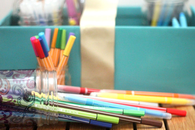 Make a super easy upcycled DIY marker storage caddy to transport the entire family's art supplies from the closet to the table in a usable bin! The jars can be removed individually to easily set up and clean up a family art station with coloring supplies for kids and adults. This recylced cardboard box and jar craft is so easy to make, and is an awesome craft room organization hack.