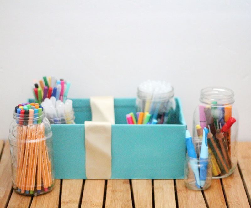 Make a super easy upcycled DIY marker storage caddy to transport the entire family's art supplies from the closet to the table in a usable bin! The jars can be removed individually to easily set up and clean up a family art station with coloring supplies for kids and adults. This recylced cardboard box and jar craft is so easy to make, and is an awesome craft room organization hack.