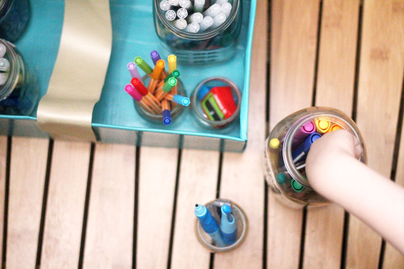 Make a super easy upcycled DIY marker storage caddy to transport the entire family's art supplies from the closet to the table in a usable bin! The jars can be removed individually to easily set up and clean up a family art station with coloring supplies for kids and adults. This recylced cardboard box and jar craft is so easy to make, and is an awesome craft room organization hack.