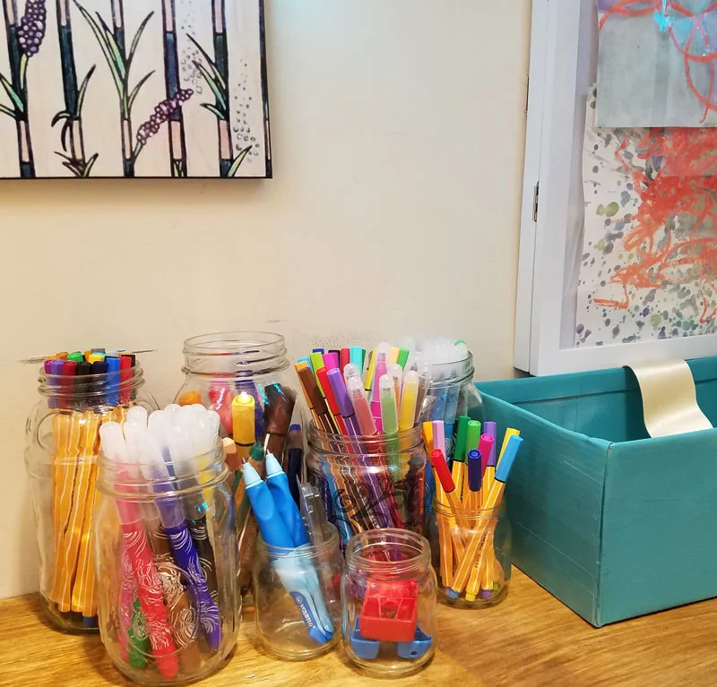 Make a super easy upcycled DIY marker storage caddy to transport the entire family's art supplies from the closet to the table in a usable bin! The jars can be removed individually to easily set up and clean up a family art station with coloring supplies for kids and adults. This recylced cardboard box and jar craft is so easy to make, and is an awesome craft room organization hack.