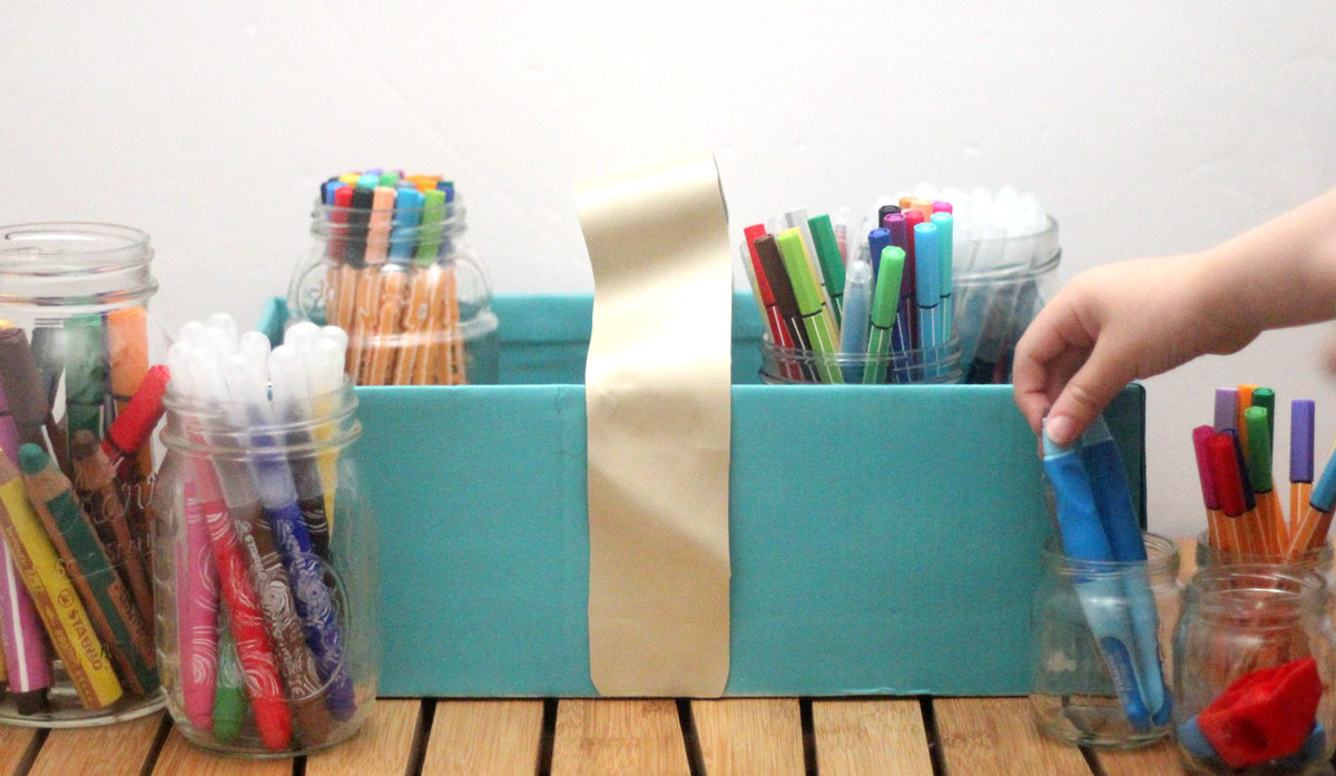 Make a super easy upcycled DIY marker storage caddy to transport the entire family's art supplies from the closet to the table in a usable bin! The jars can be removed individually to easily set up and clean up a family art station with coloring supplies for kids and adults. This recylced cardboard box and jar craft is so easy to make, and is an awesome craft room organization hack.