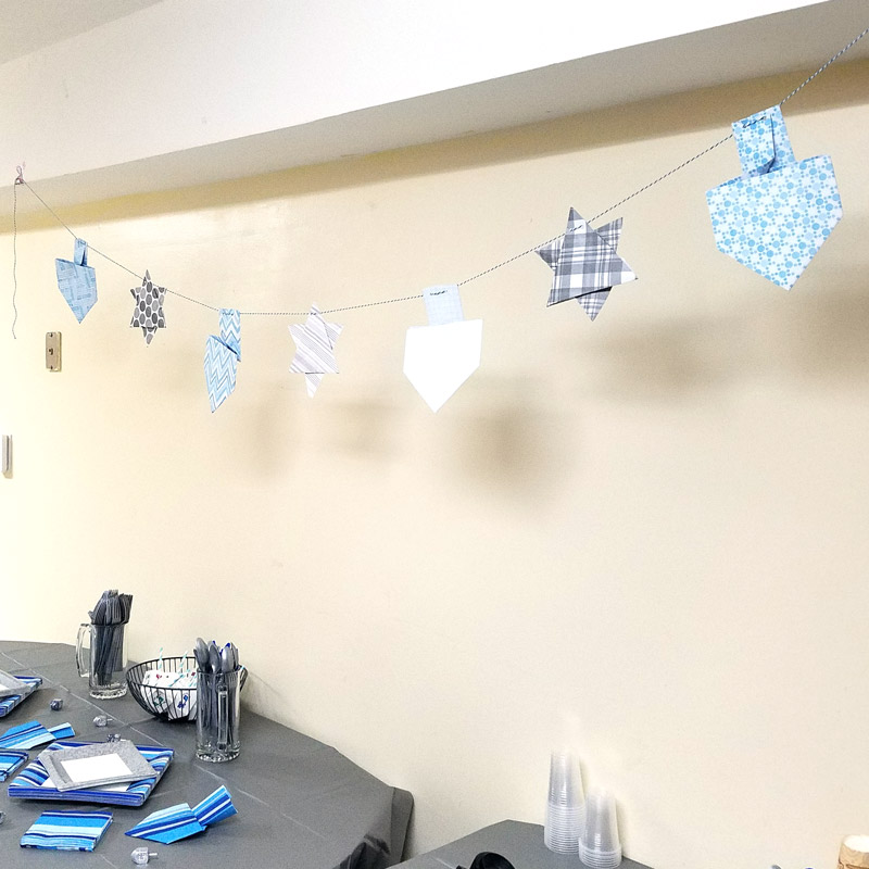 Make a fun origami Hanukkah garland featuring folded paper dreidels and star of david. This simple Chanukah craft for kids teens and adults is a perfect way to update your Hanukkah decor.