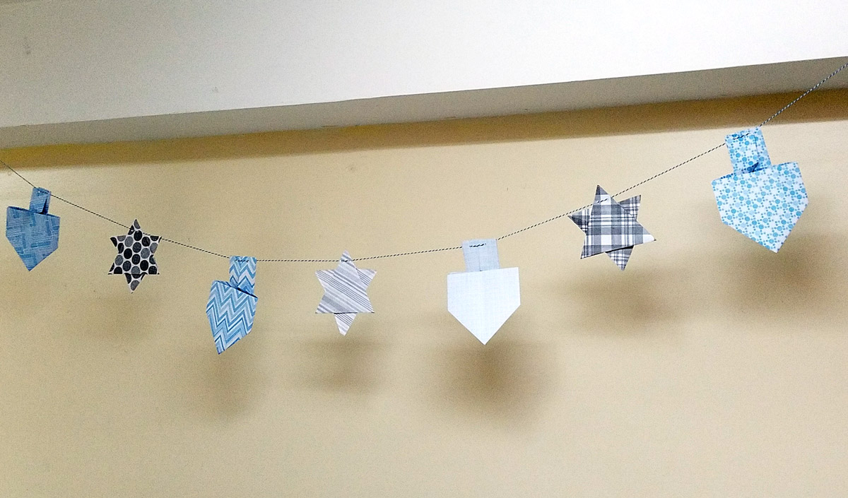 Make a fun origami Hanukkah garland featuring folded paper dreidels and star of david. This simple Chanukah craft for kids teens and adults is a perfect way to update your Hanukkah decor.