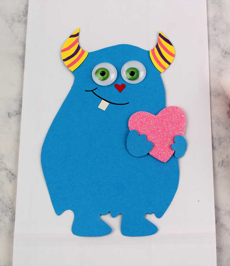 These adorable Monster love valentine treat bags are perfect for favors or snacks! This cute Valentine's Day paper craft is also good for a monster birhtday party. It doesn't have to have the heart, and you can put any shape in the monster's hands. #papercraft #valentinesday #valentine