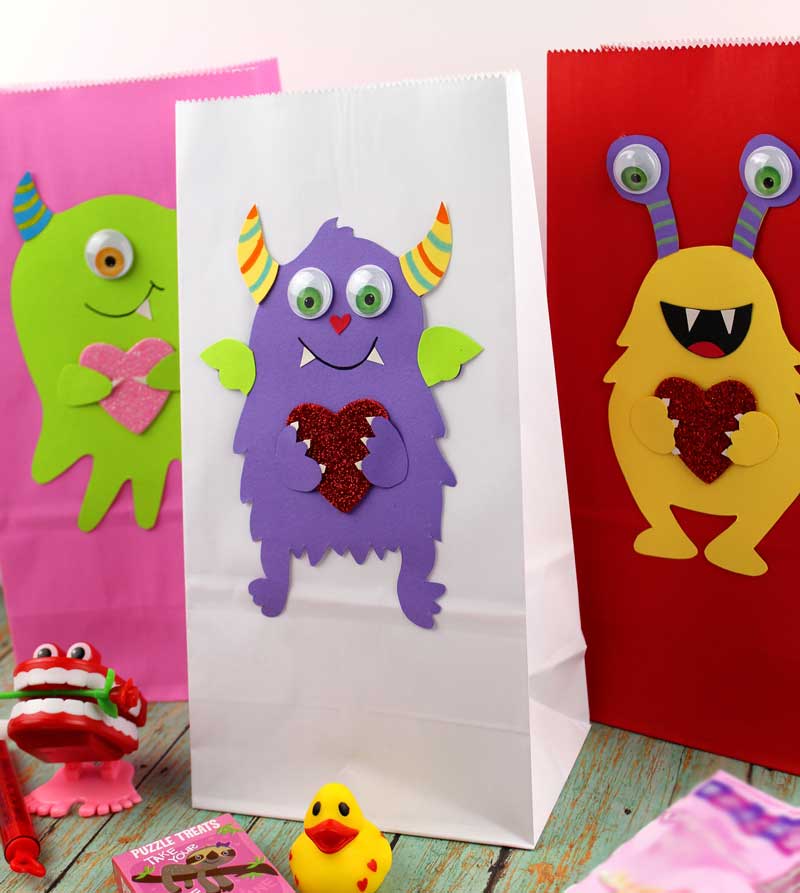 These adorable Monster love valentine treat bags are perfect for favors or snacks! This cute Valentine's Day paper craft is also good for a monster birhtday party. It doesn't have to have the heart, and you can put any shape in the monster's hands. #papercraft #valentinesday #valentine