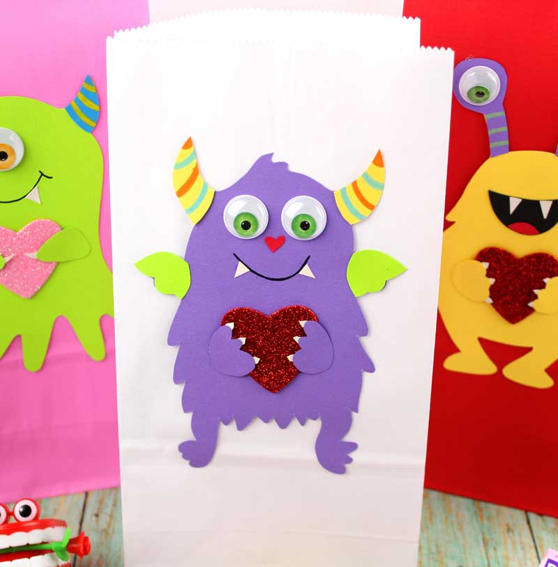 These adorable Monster love valentine treat bags are perfect for favors or snacks! This cute Valentine's Day paper craft is also good for a monster birhtday party. It doesn't have to have the heart, and you can put any shape in the monster's hands. #papercraft #valentinesday #valentine