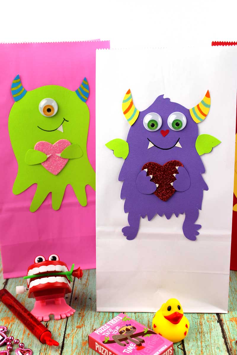 These adorable Monster love valentine treat bags are perfect for favors or snacks! This cute Valentine's Day paper craft is also good for a monster birhtday party. It doesn't have to have the heart, and you can put any shape in the monster's hands. #papercraft #valentinesday #valentine